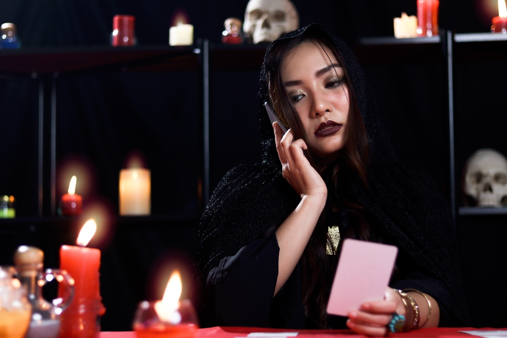 Mysterious magnificent beautiful woman fortune teller in black hood read future on card and calling to customers to tell them, online working running business.