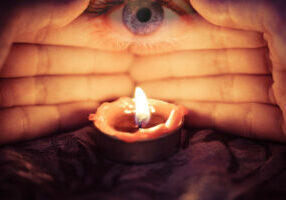 Hand with candlelight burning candle on the darkness background with the eye looking for Astrology Occult Magic illustration / Magic Spiritual Horoscopes and Palm reading fortune teller concept